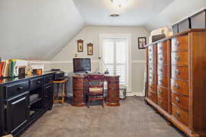 Carpeted home office with visible vents, lofted ceiling, and baseboards