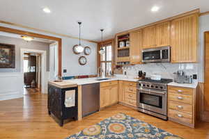 Kitchen with open shelves, appliances with stainless steel finishes, light countertops, ornamental molding, and a sink