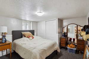 Bedroom featuring a closet, wainscoting, dark colored carpet, and a textured ceiling