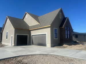 View of property exterior with a shingled roof, an attached garage, brick siding, stucco siding, and concrete driveway