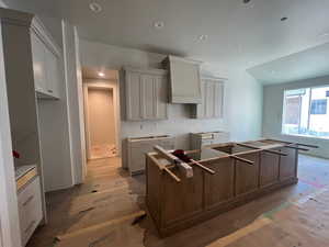 Kitchen with lofted ceiling, light wood-style floors, a center island, recessed lighting, and custom range hood