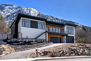 Modern home featuring a balcony, fence, a garage, concrete driveway, and a mountain view