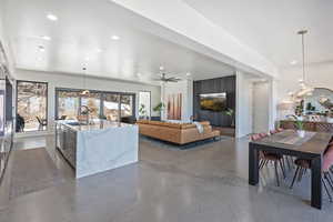 Living area featuring finished concrete flooring, ceiling fan with notable chandelier, and recessed lighting
