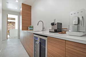Kitchen featuring finished concrete flooring, a sink, beverage cooler, modern cabinets, and brown cabinetry