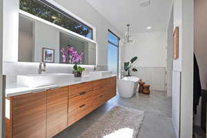Full bath with concrete flooring, double vanity, a sink, and a freestanding tub
