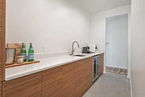 Kitchen with concrete flooring, wine cooler, a sink, modern cabinets, and brown cabinetry