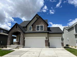 View of front of property with brick siding, concrete driveway, stucco siding, cooling unit, and roof with shingles