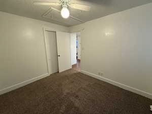 Unfurnished bedroom featuring a closet, a textured ceiling, dark colored carpet, baseboards, and ceiling fan