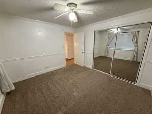 Unfurnished bedroom featuring carpet, a closet, a ceiling fan, a textured ceiling, and ornamental molding
