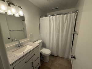 Full bathroom with tile patterned flooring, vanity, toilet, a textured ceiling, and visible vents