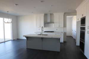Kitchen with wall chimney range hood, white cabinets, a sink, and backsplash
