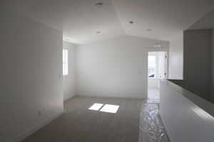 Empty room with baseboards, lofted ceiling, a wealth of natural light, and light carpet