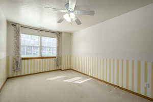Carpeted empty room with baseboards, a textured ceiling, wallpapered walls, visible vents, and a ceiling fan