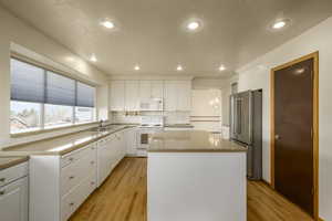Kitchen with white cabinetry, tasteful backsplash, white appliances, a center island, and light wood-style flooring