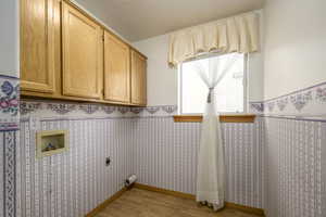 Laundry room with wallpapered walls, light wood finished floors, cabinet space, electric dryer hookup, and wainscoting