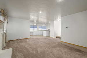 Unfurnished living room with built in desk, light colored carpet, baseboards, a textured ceiling, and a ceiling fan