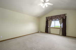 Spare room featuring light colored carpet, a ceiling fan, baseboards, and vaulted ceiling