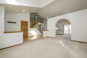 Unfurnished living room with a chandelier, baseboards, stairway, arched walkways, and carpet floors