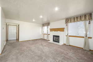 Unfurnished living room with a fireplace with flush hearth, carpet floors, a textured ceiling, and baseboards