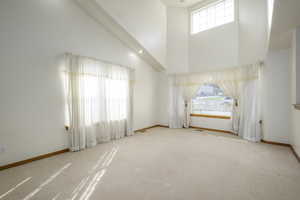 Carpeted empty room featuring baseboards, a high ceiling, and a healthy amount of sunlight