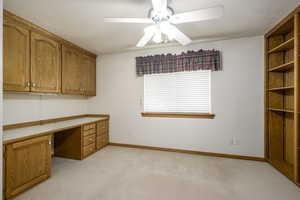Unfurnished office with light carpet, baseboards, a ceiling fan, and built in study area