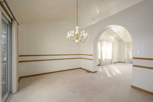 Carpeted empty room featuring arched walkways, baseboards, a chandelier, and visible vents