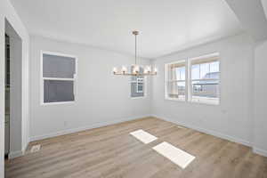 Spare room with baseboards, visible vents, light wood-type flooring, and a notable chandelier