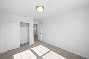 Unfurnished bedroom with baseboards, a closet, light colored carpet, and visible vents