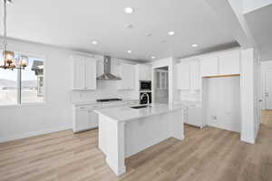 Kitchen featuring black cooktop, stainless steel microwave, a center island with sink, a sink, and wall chimney range hood