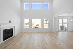 Unfurnished living room with baseboards, a high ceiling, light wood-style flooring, and a brick fireplace