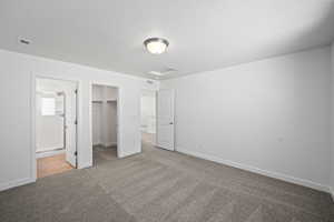Unfurnished bedroom featuring a walk in closet, carpet, a textured ceiling, visible vents, and a closet