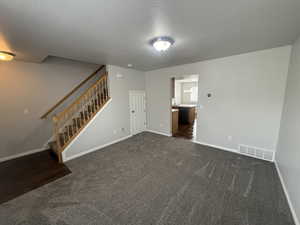 Unfurnished living room with stairs, visible vents, dark carpet, and baseboards