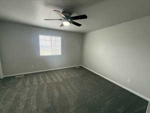 Unfurnished room with baseboards, a textured ceiling, dark carpet, visible vents, and a ceiling fan