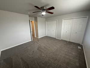 Unfurnished bedroom with two closets, dark carpet, baseboards, and visible vents