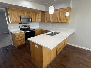 Kitchen featuring a sink, light countertops, a peninsula, appliances with stainless steel finishes, and dark wood-style floors
