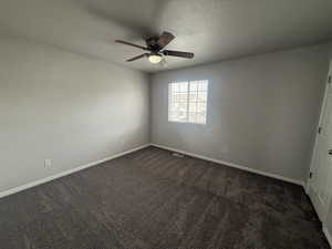 Spare room featuring baseboards, visible vents, dark colored carpet, and ceiling fan