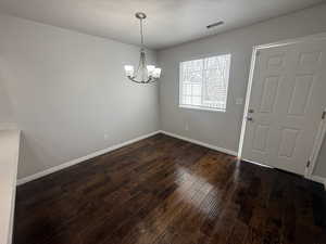 Interior space with baseboards, visible vents, a notable chandelier, and dark wood finished floors