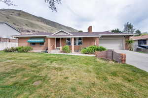 Ranch-style house featuring a front yard, brick siding, concrete driveway, and a chimney