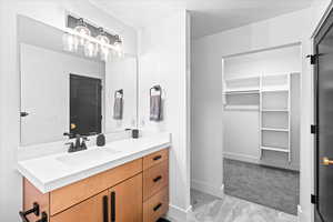 Bathroom with marble finish floor, vanity, a walk in closet, and baseboards