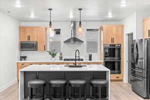Kitchen with light countertops, wall chimney range hood, light brown cabinetry, and appliances with stainless steel finishes