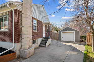 View of side of home with an outdoor structure, concrete driveway, fence, brick siding, and a garage