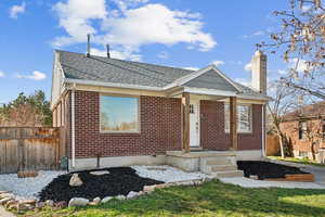 Bungalow featuring brick siding, fence, a chimney, and roof with shingles