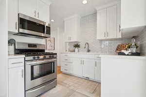 Kitchen featuring white cabinetry, light countertops, decorative backsplash, a sink, and appliances with stainless steel finishes