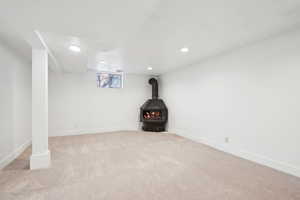 Below grade area with baseboards, a wood stove, recessed lighting, and light colored carpet