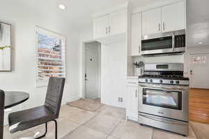 Kitchen with white cabinets, light tile patterned flooring, stainless steel appliances, and a wealth of natural light