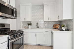 Kitchen featuring light countertops, tasteful backsplash, stainless steel appliances, a sink, and white cabinets