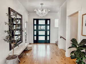 Entrance foyer with baseboards, stairs, an inviting chandelier, and light wood-type flooring