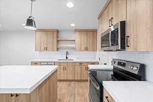 Kitchen featuring light wood finished floors, appliances with stainless steel finishes, a sink, open shelves, and light brown cabinetry