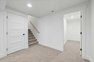 Below grade area with light colored carpet, visible vents, baseboards, and recessed lighting