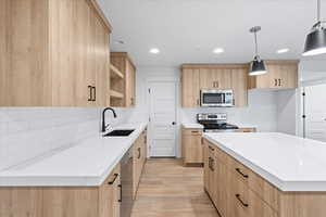 Kitchen featuring a sink, stainless steel appliances, light brown cabinetry, and light wood-style floors